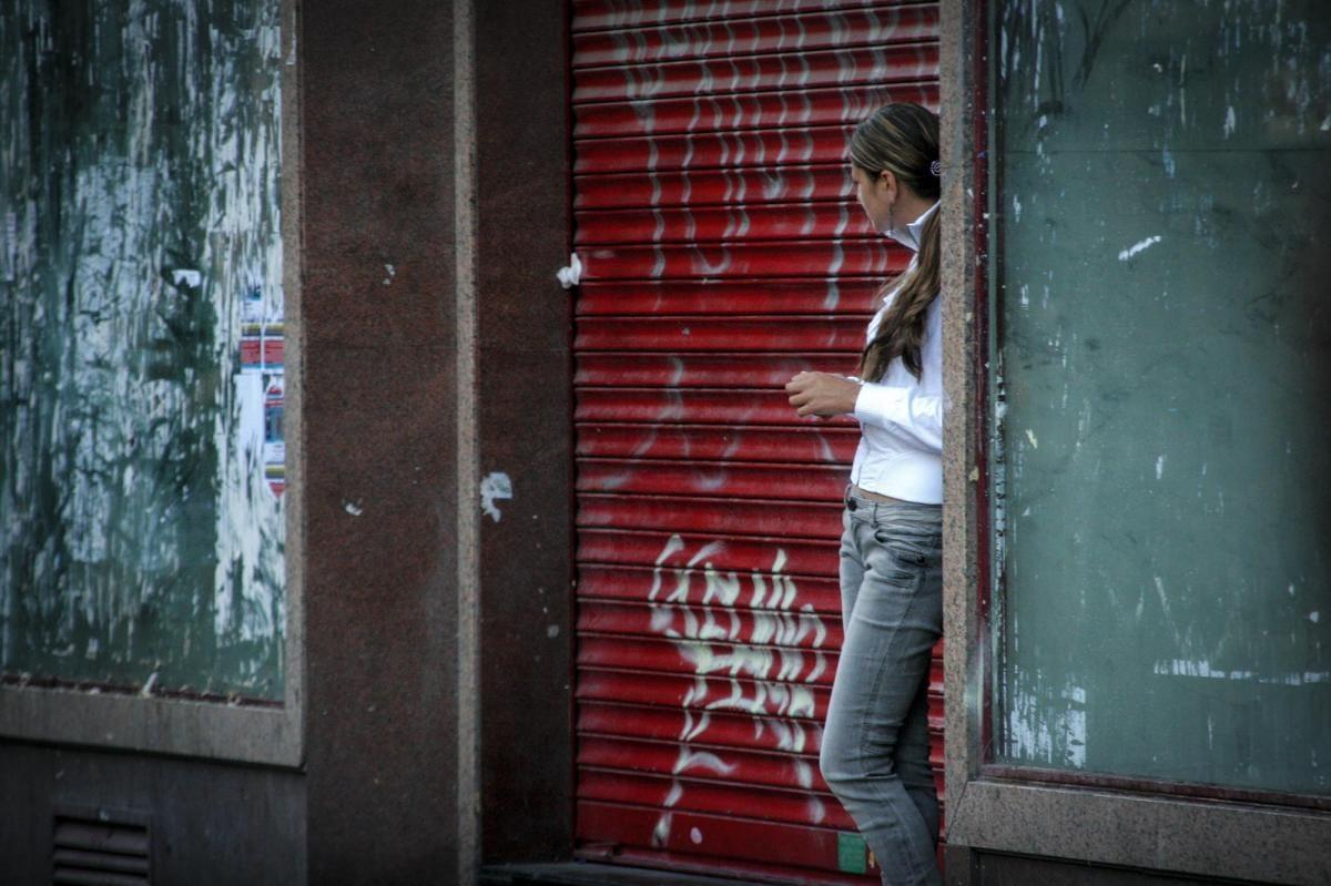 Mujer apoyada en un local con la persiana bajada Día Internacional contra Explotación Sexual y Trata
